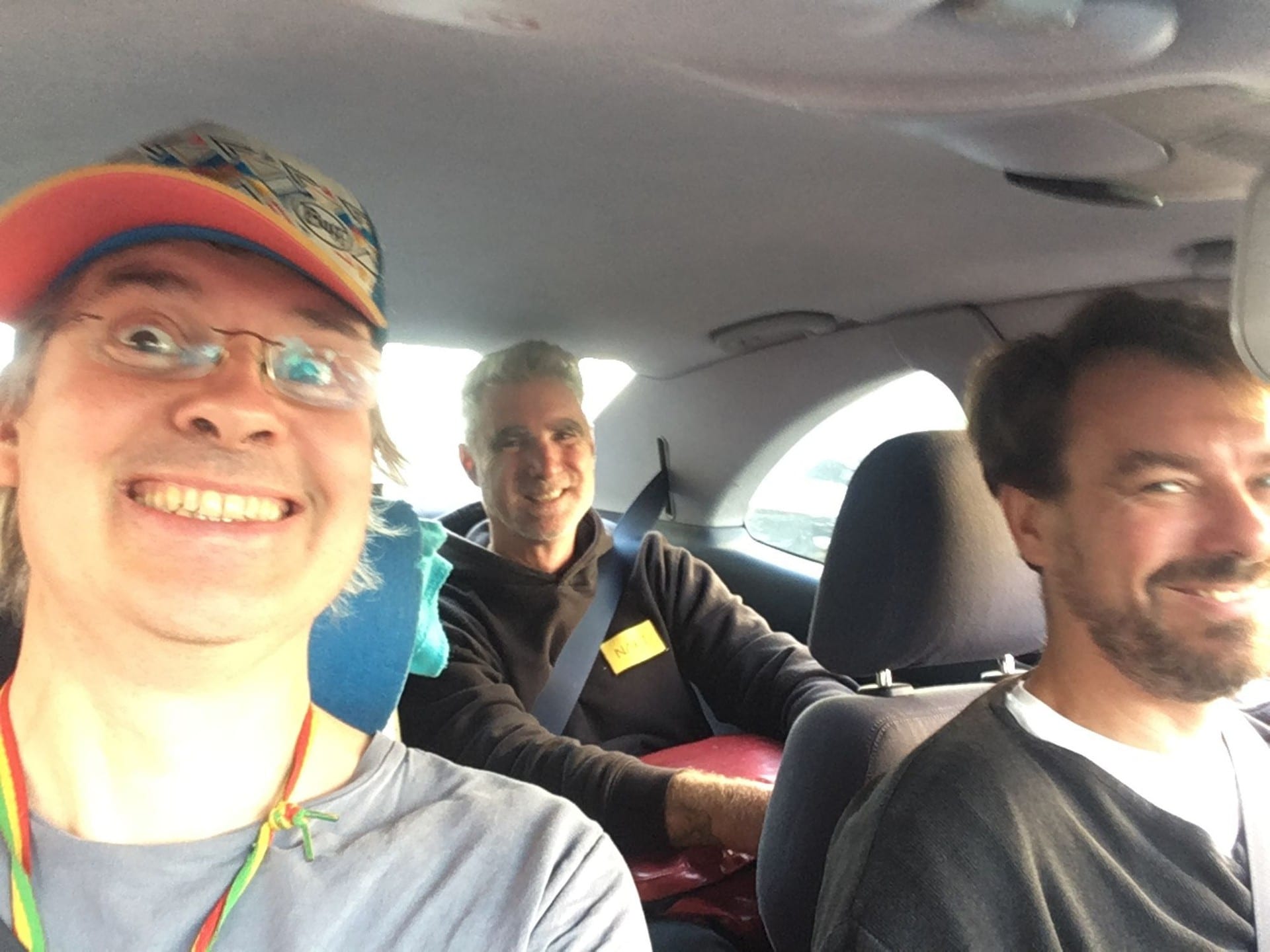 Three people in a car, the driver and passengers grinning at a phone held up for a selfie