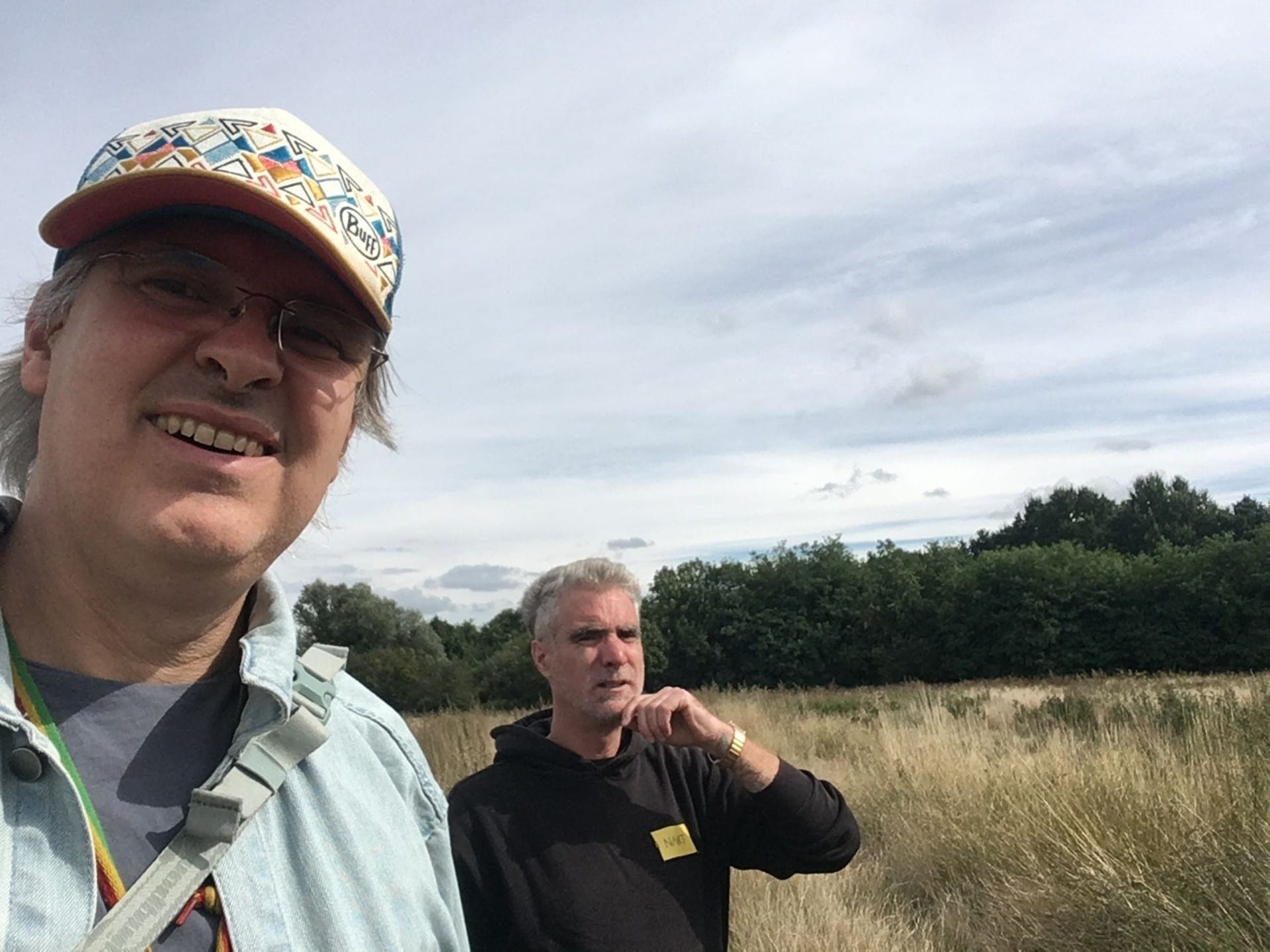 Two men in a grassy field under a cloudy sky, one taking the photograph
