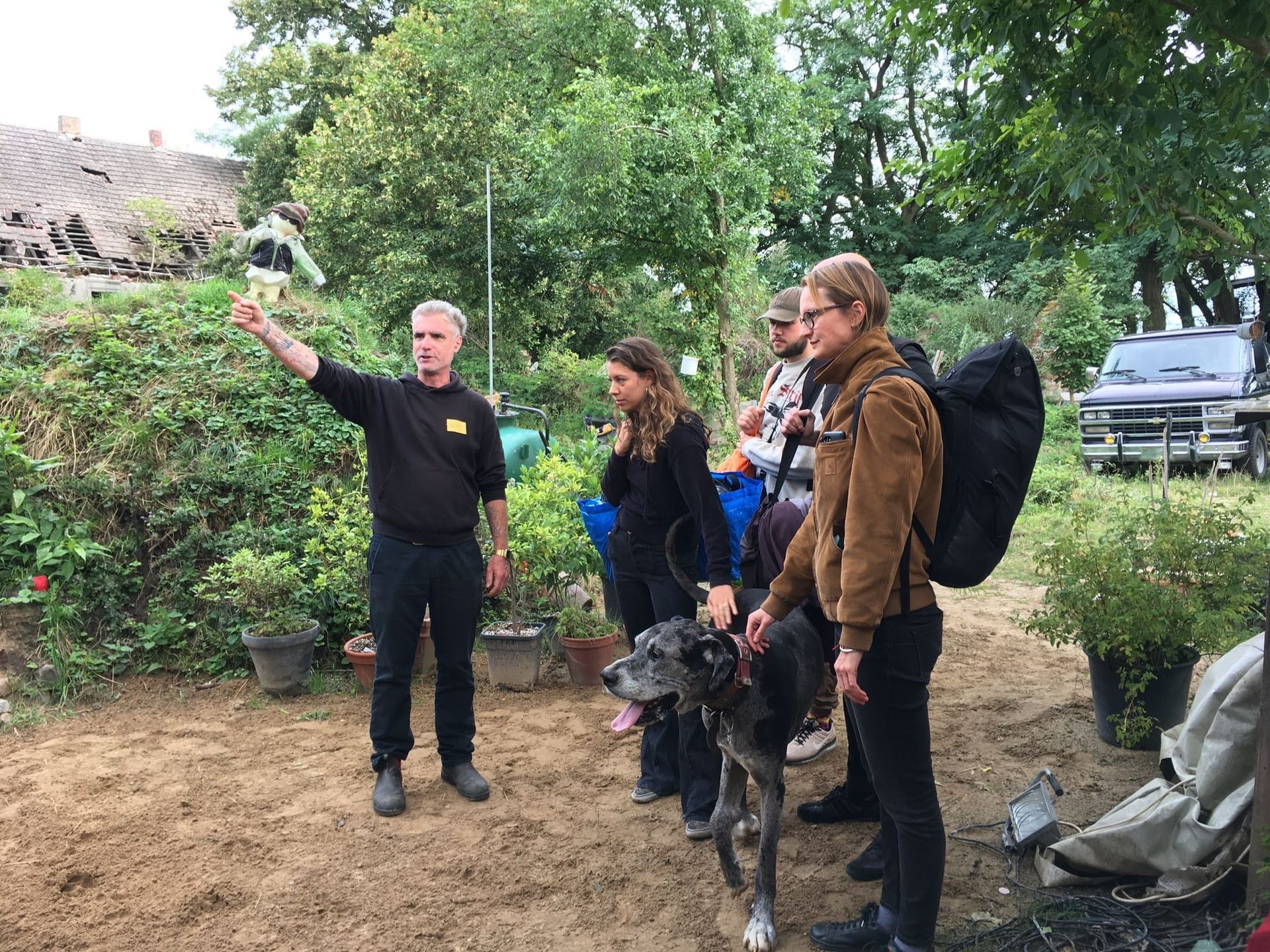 A man pointing something out to a small group in a farmyard, a great dane standing with them